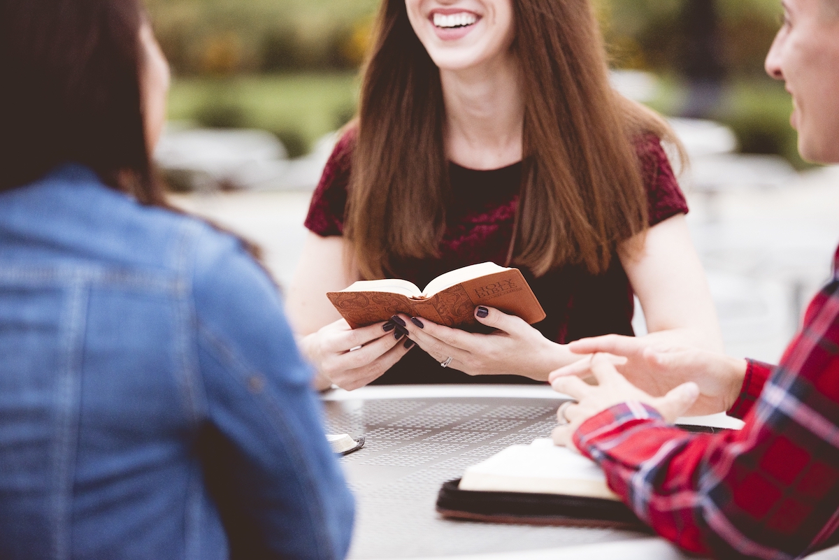 A closeup shot of females sitting around a table and reading the holy bible with a blurred background